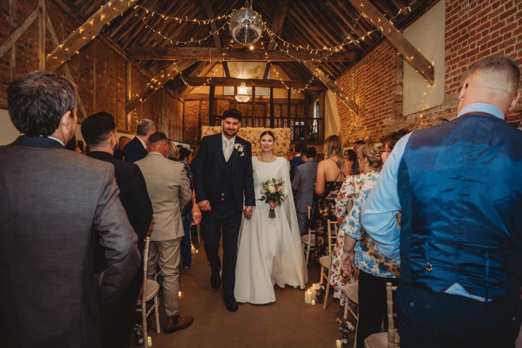 Newlyweds walking down aisle in rustic venue.