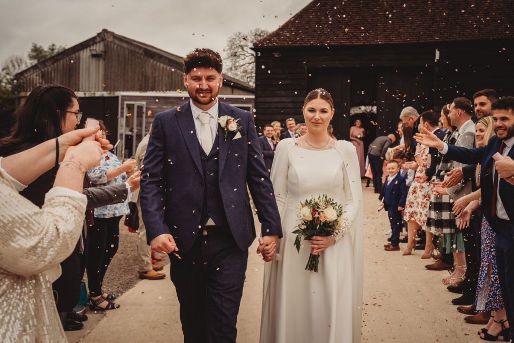 Newlyweds walk through confetti at outdoor wedding ceremony.