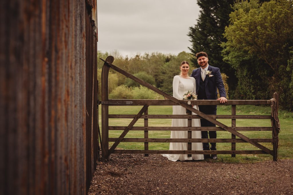 Bride and groom by rustic wooden gate.