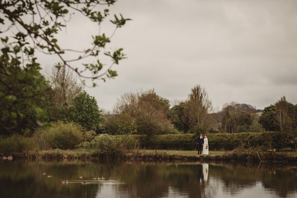 Couple standing by lake in scenic countryside setting.