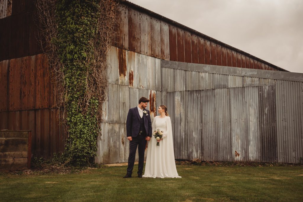 Bride and groom standing by rustic barn