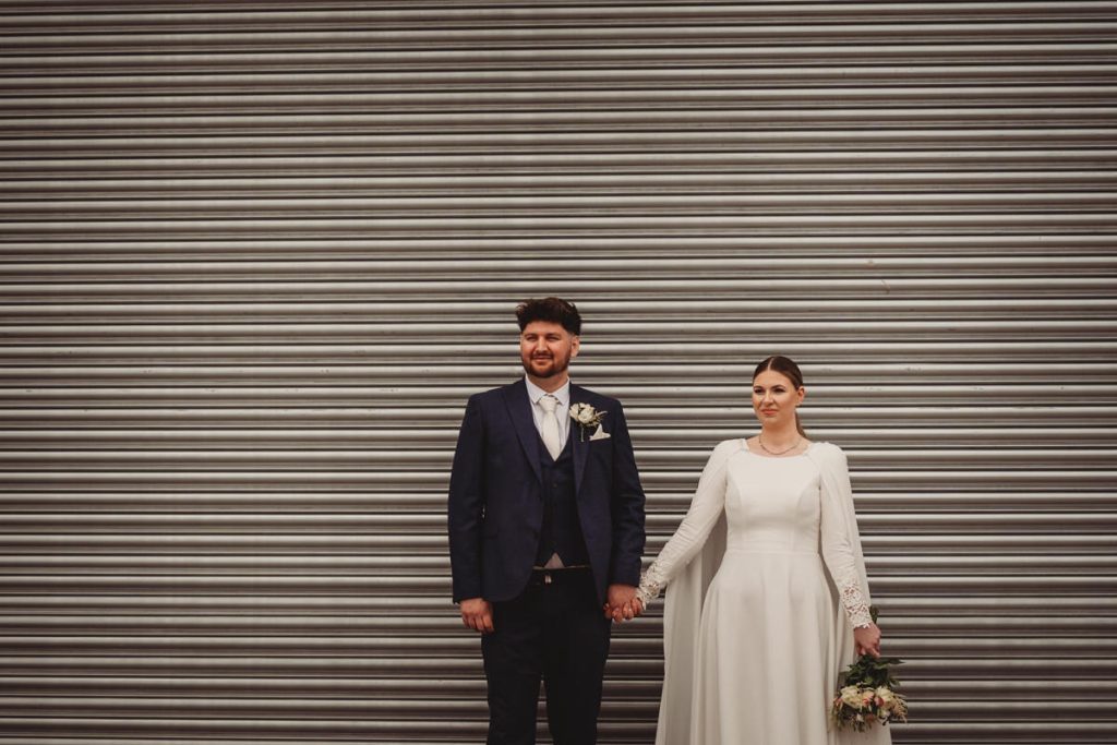 Wedding couple holding hands, grey shutter background.