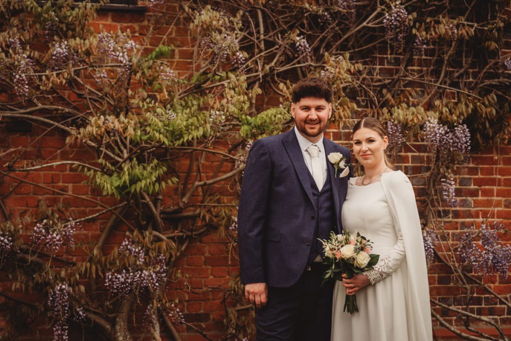 Bride and groom in front of flowering wall.