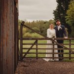 Bride and groom by a wooden gate outdoors.