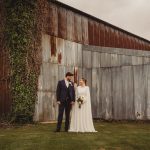 Bride and groom stand by rustic metal barn.