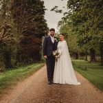 Bride and groom on tree-lined path.