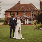 Couple in wedding attire outside brick house