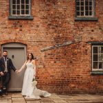 Newlyweds holding hands with dog at brick building.