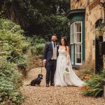 Bride and groom with dog outside rustic venue.