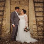 Bride and groom smiling against stone wall