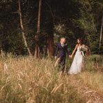 Bride and groom walking in a forest clearing.