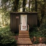 Wedding dress hanging outside rustic cabin in woods.