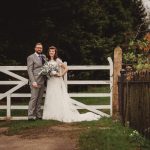 Bride and groom pose by white gate.