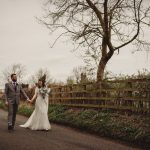 Newlyweds walking down a country lane, holding hands.