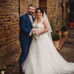 Bride and groom smiling by stone wall.