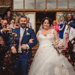 Newlyweds exit ceremony, surrounded by joyful guests.