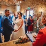 Couple getting married in rustic venue with guests watching.