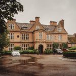 Historic brick manor with parked cars and greenery.