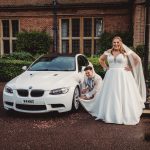 Bride, groom pose with white BMW car.