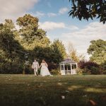 Bride and groom walk near garden gazebo.