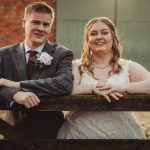 Bride and groom smiling near wooden gate.