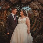 Bride and groom under rustic, lit archway.