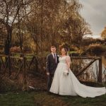 Bride and groom on rustic bridge in countryside.