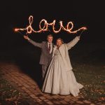 Newlyweds holding sparklers write 'love' in darkness.