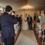 Bride walking down aisle with guests watching.