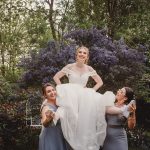 Bride lifted by two bridesmaids in garden setting.