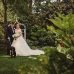 Bride, groom, and dog in garden wedding scene.