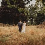 Couple walking in meadow holding hands, wedding attire.