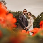 Bride and groom in garden with red flowers.