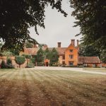 Historic manor house surrounded by gardens and trees.