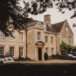 Historic manor house with parked cars in driveway.