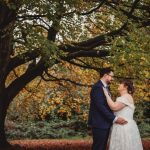 Couple under autumn tree during wedding ceremony.