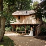 Couple standing by elevated wooden treehouse in forest.