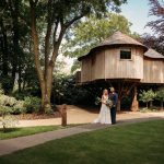 Couple posing in front of a wooden treehouse.