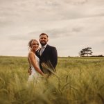 Couple standing in a green field, smiling.