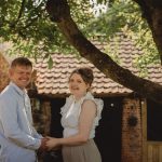 Smiling couple holding hands under a tree.