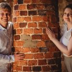 Couple smiling behind a brick pillar.