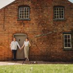 Couple holding hands outside brick cottage.