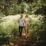 Couple walking hand-in-hand on forest path.