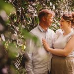 Couple smiling in a leafy garden setting.