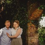 Couple smiling near ivy-covered brick archway.