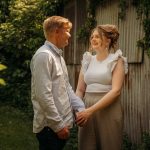 Couple holding hands, smiling in garden setting.