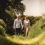 Couple walking hand in hand through lush path.