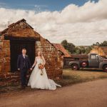 Bride and groom by rustic barn with vintage truck.