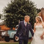 Bride and groom smiling, holding hands outdoors.