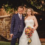 Couple in wedding attire under a tree, smiling.